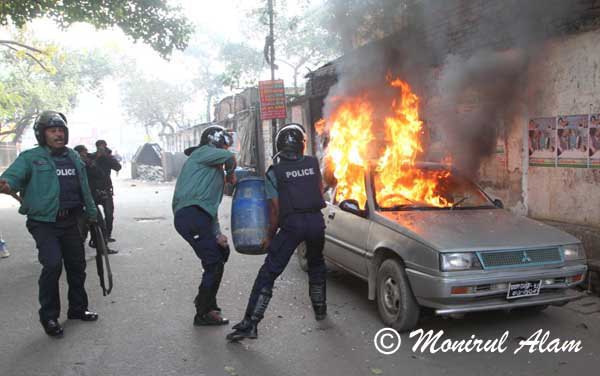 A Bangladeshi  polices carries a water drum to  try to remove  fires on the burning car during