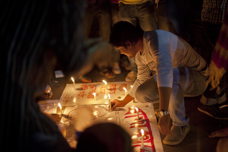A protester places a candle next to handmade posters with caricatures of those accused of war crimes. Credit: Shahidul Alam/Drik/Majority World