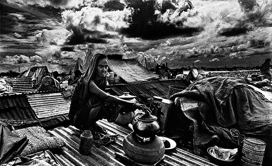 Surrounded by her worldly goods a woman cooks for her family on a rooftop shelter during the 1988 floods. ? Shahidul Alam/Drik/Majority World